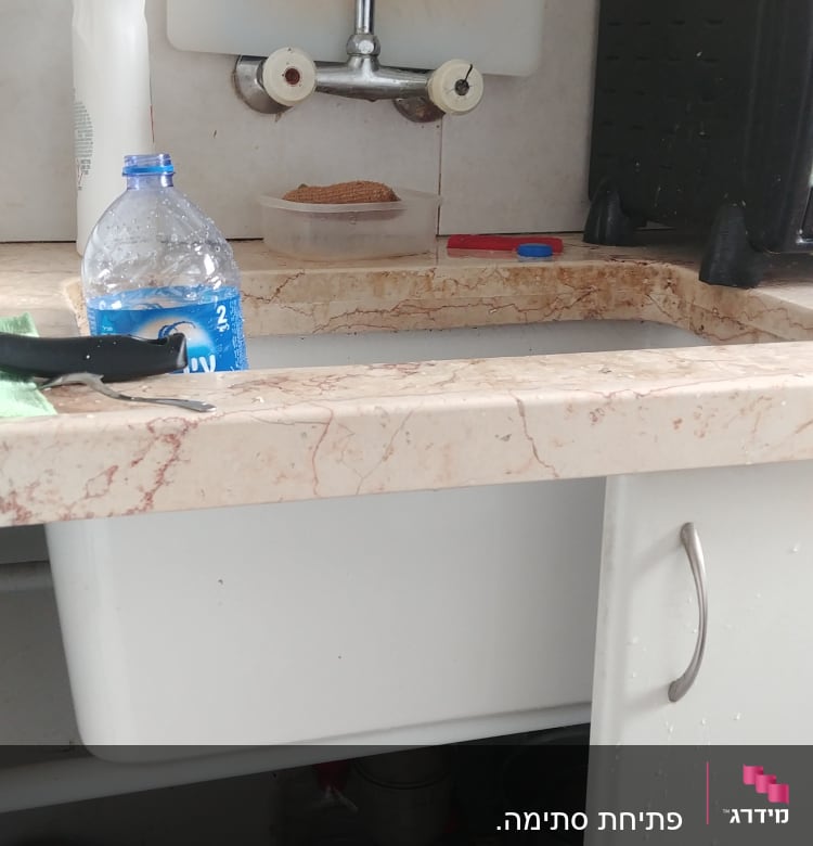 כיור מטבח עם ברז, בקבוק מים וכלים מתחת לכיור